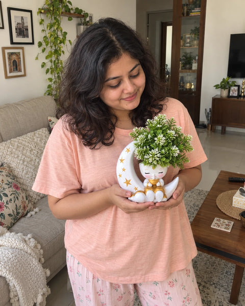 Woman smiling at the MiniKin Festival Moon Planter with its artificial plant in a living room